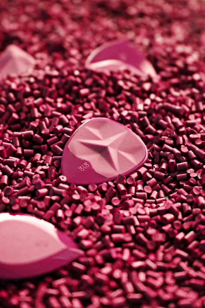 Vibrant pink guitar picks resting on a bed of colorful plastic granules.
